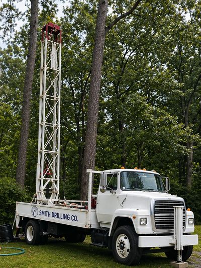 White drilling truck from Smith Drilling Co. parked near trees.