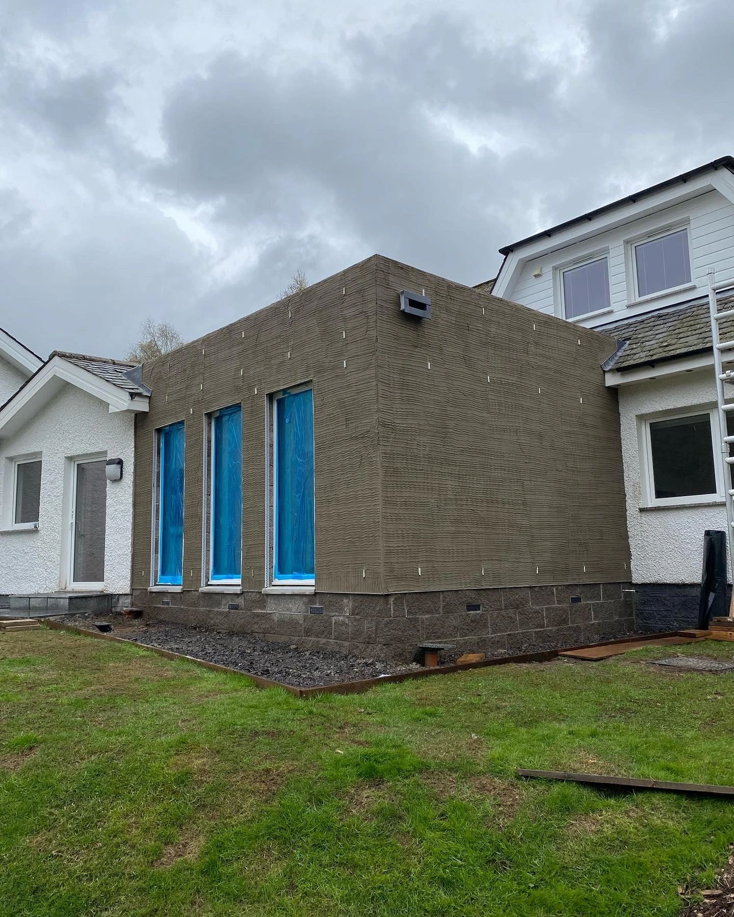 House extension under construction with 3 tall windows and textured exterior walls.