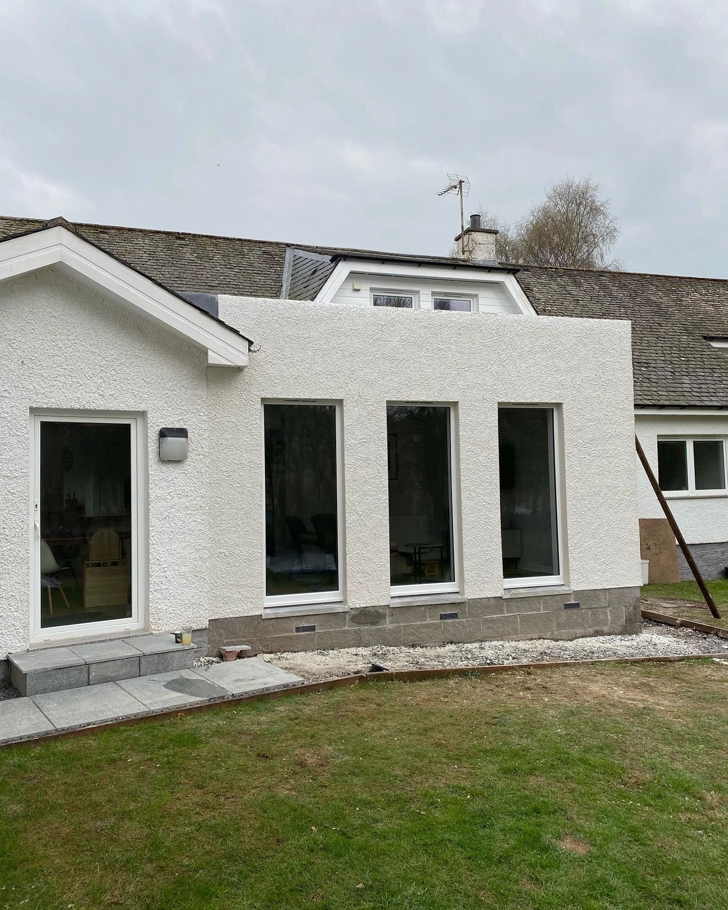 White stucco house exterior with large windows and a small stone patio area.