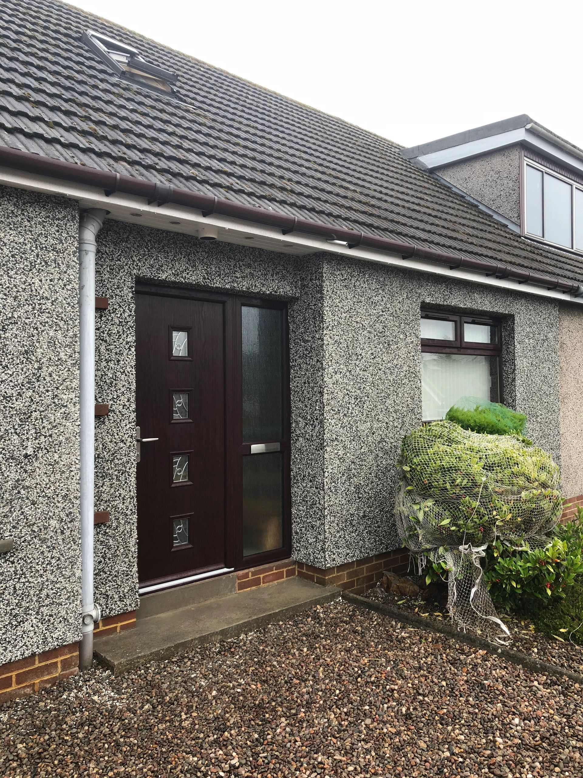 Exterior of a house with a dark wooden door and pebbled driveway.
