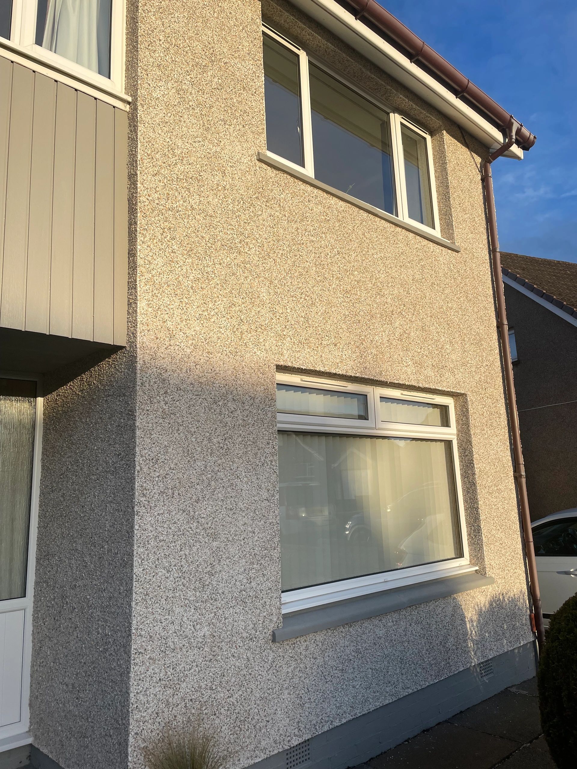 Two-story house exterior with textured walls and white-framed windows.