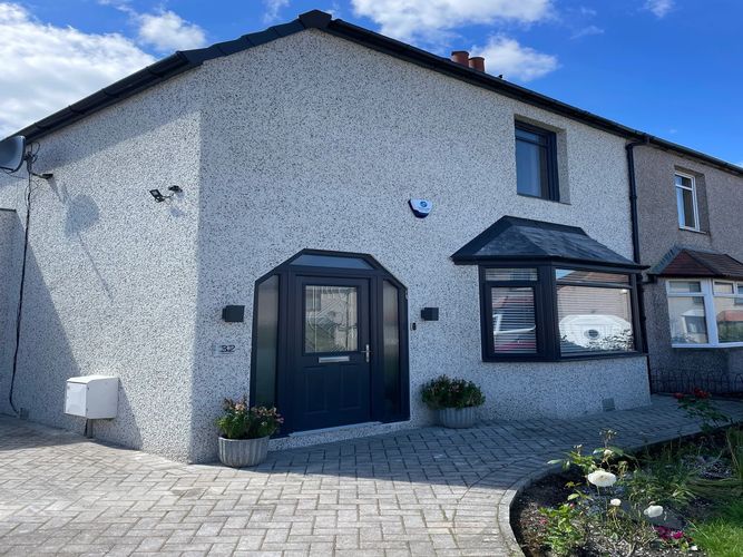 Modern house entrance with a dark door and bay window under a clear blue sky.
