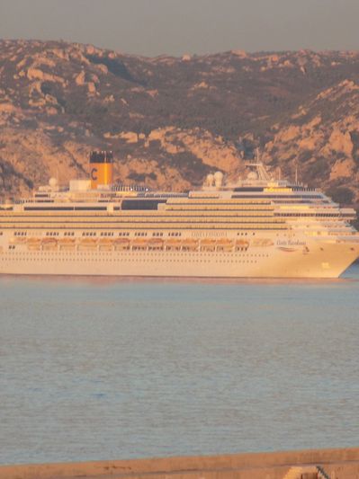 Large cruise ship sailing near rocky coastline during sunset.