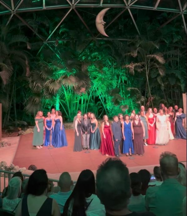 Group of performers singing on stage in elegant dresses and suits.