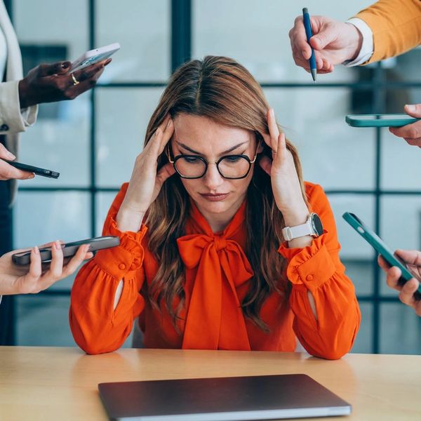 Stressed woman in glasses overwhelmed by multiple phone calls.