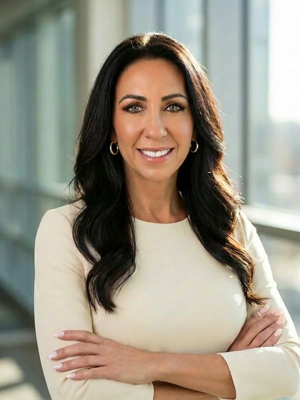 Confident woman with long dark hair and a cream dress smiling indoors.