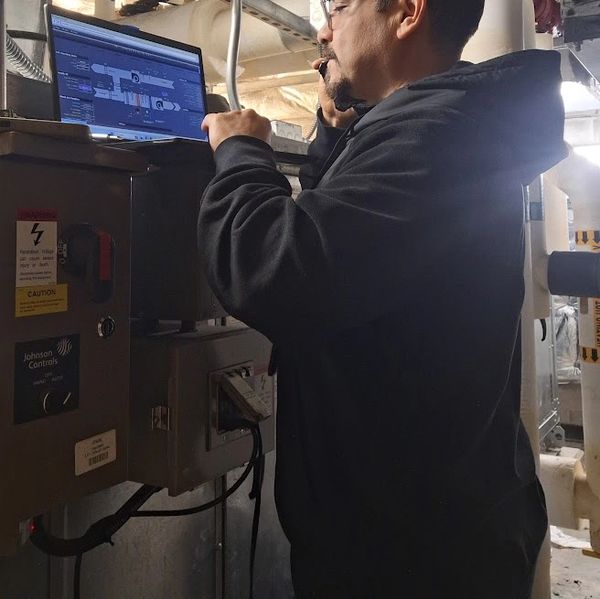Technician uses laptop and phone to monitor industrial control systems.