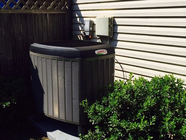 A Lennox air conditioning unit outside a house near bushes.