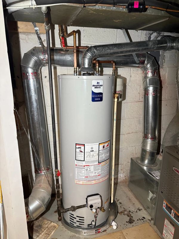 A Bradford White water heater installed in a basement with connected ductwork and pipes.