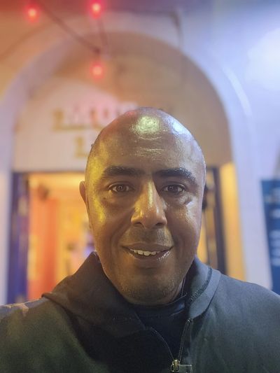 Smiling man taking a close-up selfie in a warmly lit environment.