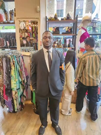 Man dressed in a suit standing in a clothing store surrounded by colorful scarves and shoes.
