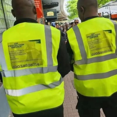 Two security guards wearing high-visibility jackets walking down a street.
