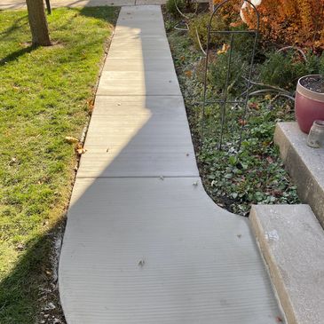 A freshly paved concrete sidewalk running past a lawn and steps.