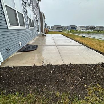 Newly poured concrete patio beside a house on a cloudy day.