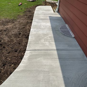 Newly poured concrete sidewalk beside a red house.