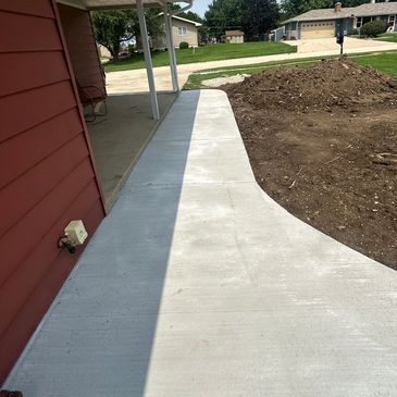 Newly poured concrete sidewalk along a red house.