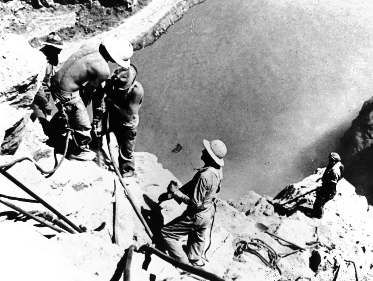 Workers with safety helmets working on rocky terrain near water.