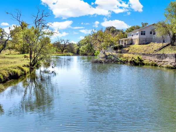 Calm river flowing beside a house under a bright blue sky.