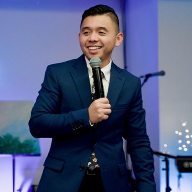 Man in navy suit holding a microphone and smiling.