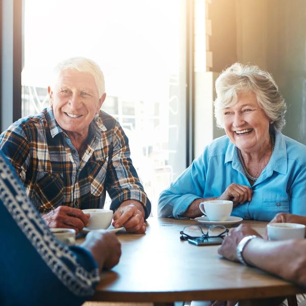 Elderly friends chatting over coffee and smiling.