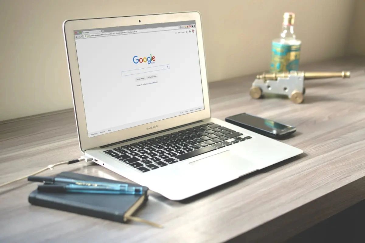 MacBook Air displaying Google homepage on a wooden desk with notebook and phone.