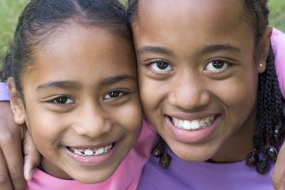 A close-up of two young girls, that must be sisters, smiling. They are wearing pink and purple. 
