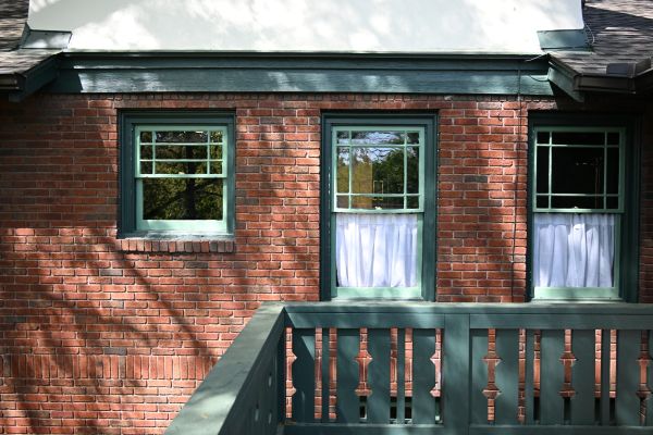 Exterior view of a brick wall with three green-trimmed windows and a green railing.