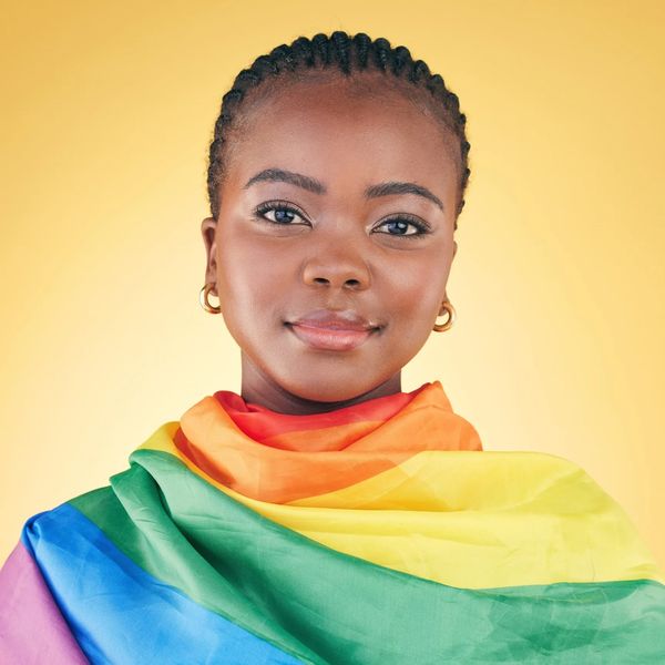 Confident woman wrapped in a vibrant rainbow pride flag, symbolizing LGBTQ+ pride.