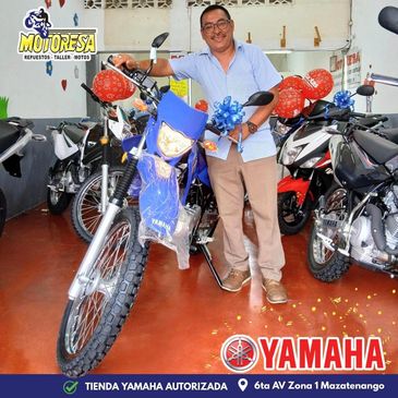 Man posing with a Yamaha motorcycle inside a showroom decorated with balloons.