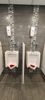 Two urinals with bottle holders installed above them in a restroom.