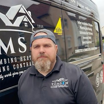 A man stands in front of a plumbing and heating contractor van.