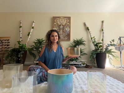 Woman sitting on the floor meditating with crystal bowls.