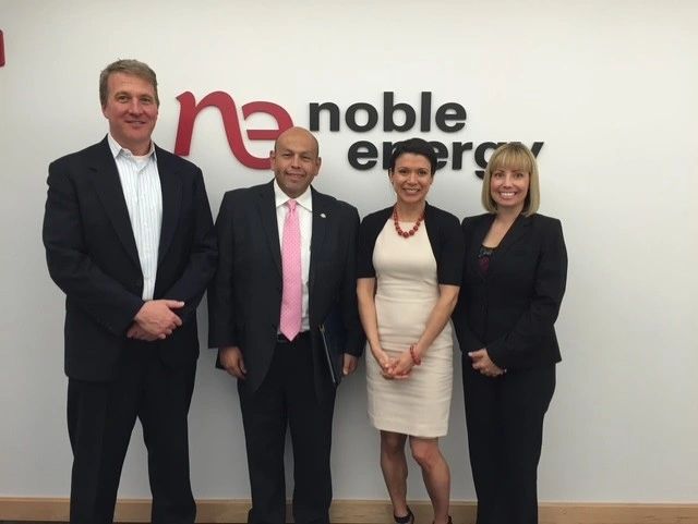 Four professionals pose in front of a Noble Energy sign in business attire.