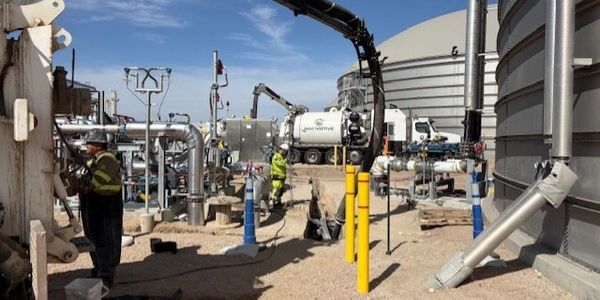 Workers operating machinery at an industrial plant with storage tanks and pipes.