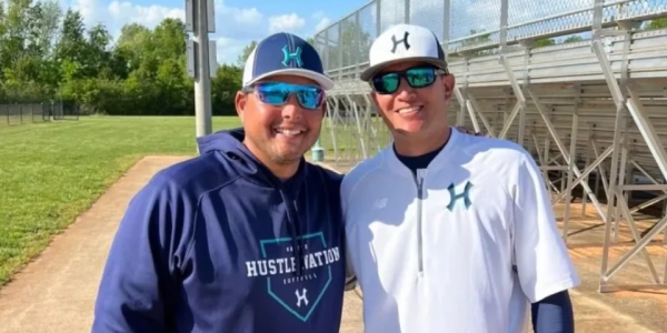Two men in baseball attire smiling at a baseball field.