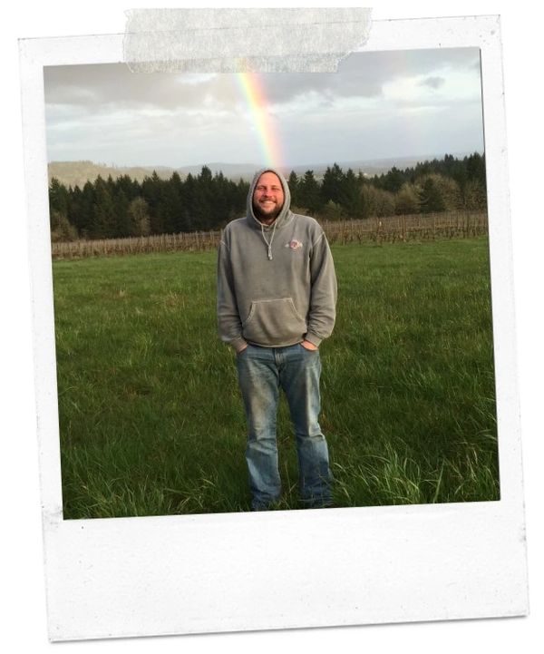 Man stands in tall grass smiling because of a rainbow.