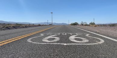 Route 66 emblem painted on an open desert road under a clear blue sky.