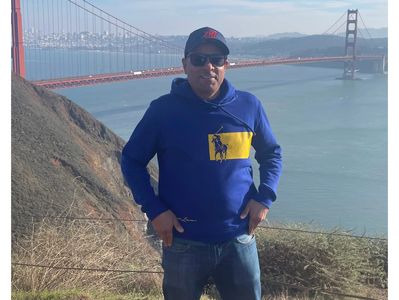 Man in blue hoodie posing near Golden Gate Bridge in San Francisco.