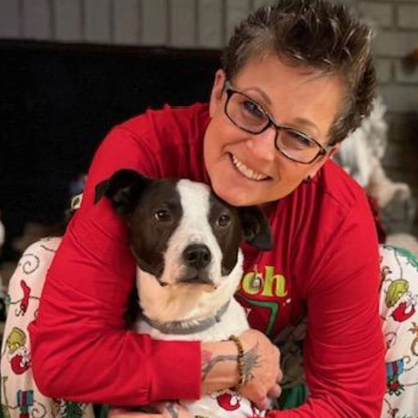 Person in glasses hugs a black and white dog, both looking at the camera.
