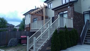 Elevated wooden deck with stairs and pergola in a backyard.