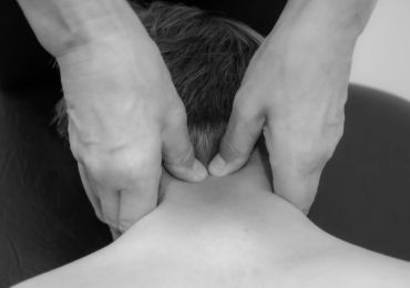 Hands giving a neck massage to a person lying face down.