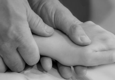 An adult hand gently holding a child's hand in black and white.