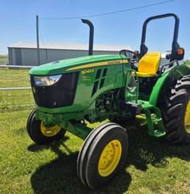 Green John Deere tractor parked on grass near a fence.