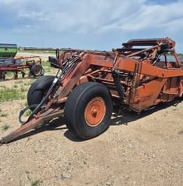Rusty orange farm equipment with large tires on a dirt field.