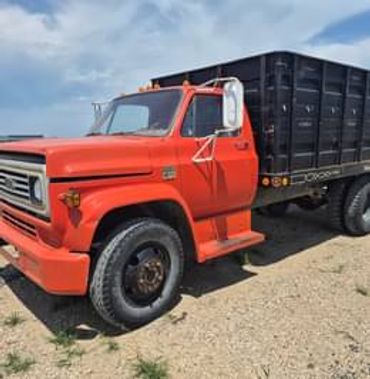 Vintage orange flatbed truck with black cargo bed on gravel.