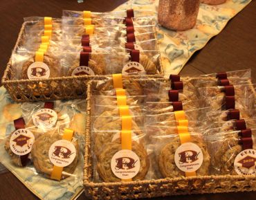 Assorted packaged cookies in baskets with ribbons and labels.