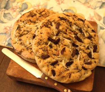 Two round herb and olive focaccias on a cutting board.