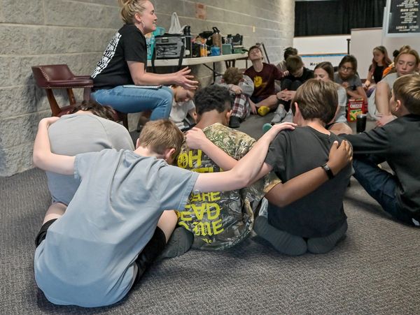 A group of children sitting in a circle with arms around each other during a discussion or group activity.