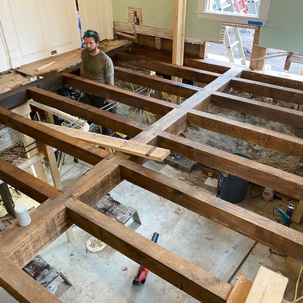 Man working on house floor renovation with exposed wooden beams.