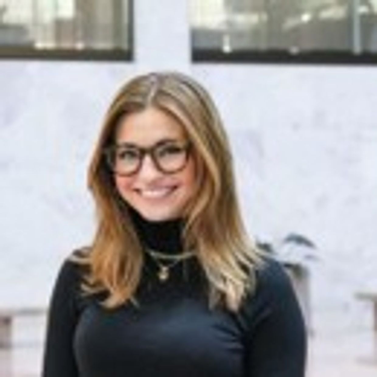 Young woman smiling, wearing glasses and a black top.